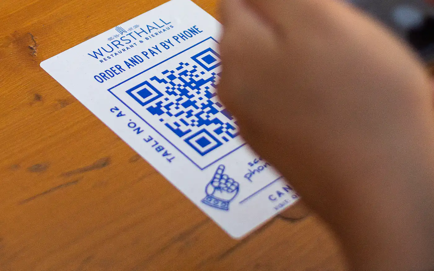 Рука с телефоном наводит камеру на карточку с QR-кодом, лежащую на деревянном столе